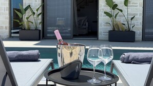 Zona junto a la piscina con sillones de descanso, una bandeja con botella y vasos, y plantas en macetas.