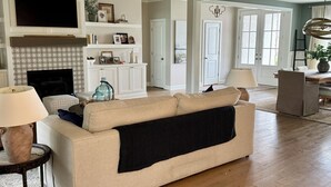 Ein Wohnzimmer mit beiger Couch, Kamin, Fernseher und Essbereich mit Tisch und Stühlen.