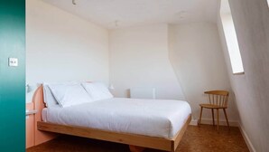 Ein Schlafzimmer mit einem Holzbett, einem kleinen Stuhl, einem Nachttisch und einem Fenster.