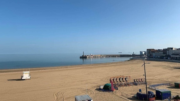 Ein Strand mit einem Rettungsturm, einer Pier und Gebäuden im Hintergrund.