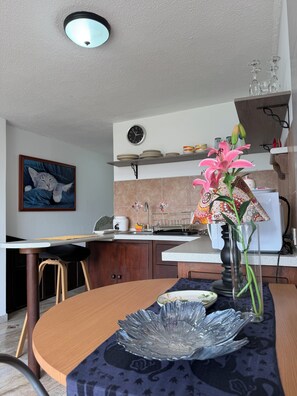A modern kitchen with a dining area, a clock, and a vase with flowers. - Charming & Cozy Suite in Quito with Great Location (Quito)