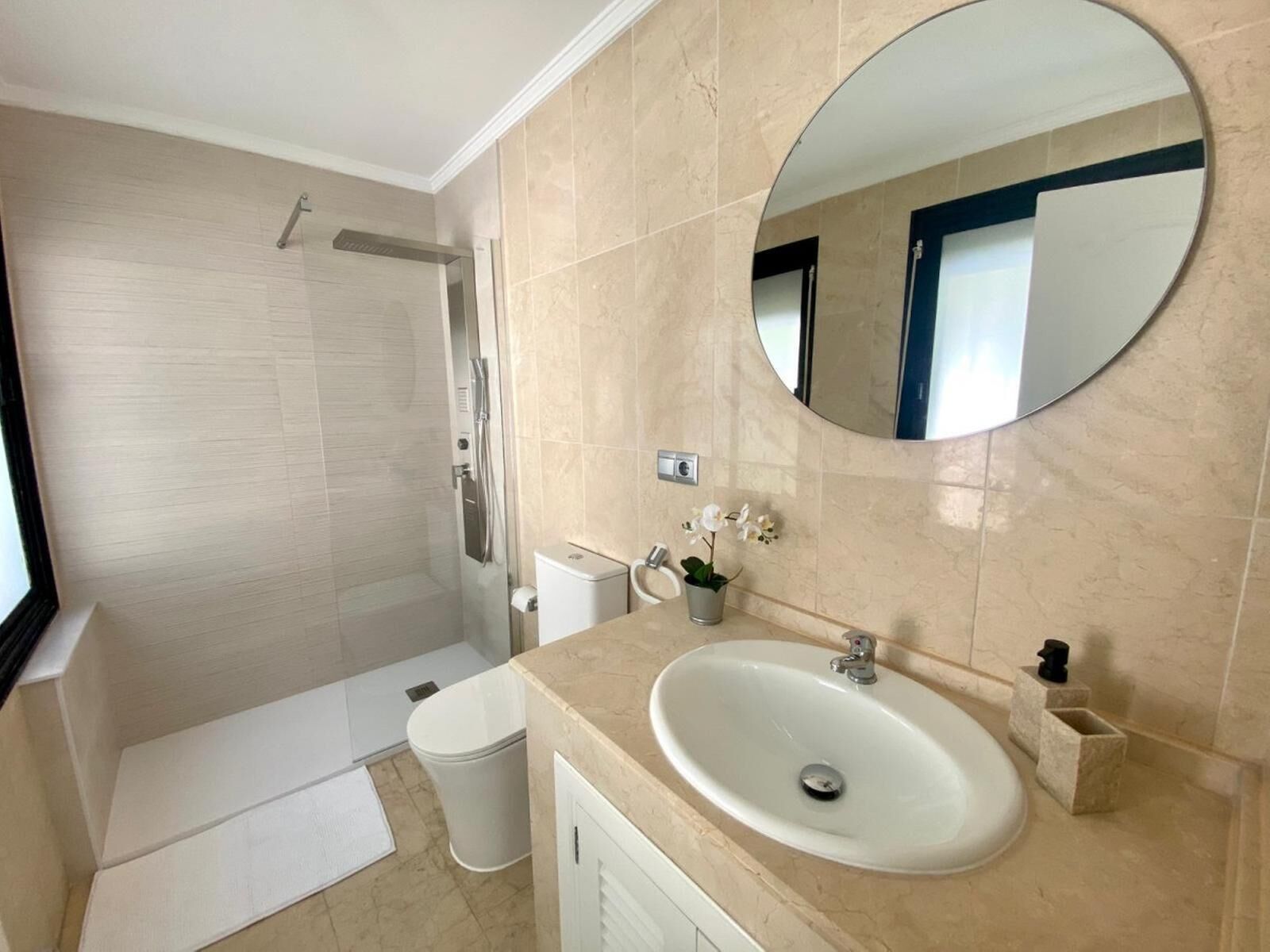 A bathroom with a shower, toilet, sink, and a large mirror.