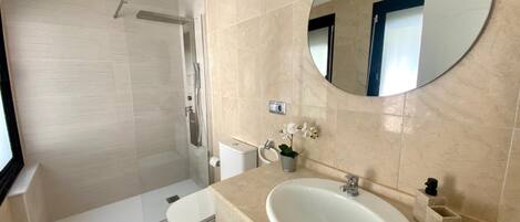 A bathroom with a shower, toilet, sink, and a large mirror.