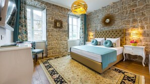 A bedroom with a stone wall, a bed with a tufted headboard, a hanging light fixture, and a bedside table with a flower vase. - Dominus Rooms  (Dubrovnik)