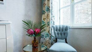 A room with a chair, a small table with a vase, and a window with curtains. - Dominus Rooms  (Dubrovnik)