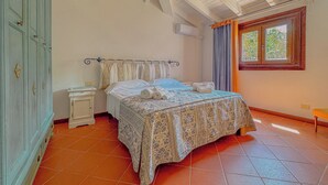 A bedroom with a bed, a nightstand, a wardrobe, and a window with curtains. - Villa Camilla: Private Pool & BBQ, Panoramic Garden Near Le Saline beach (Punta de Su Turrione)