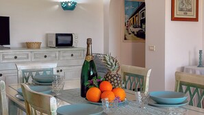 A dining table set with blue plates, a bottle of champagne, and a pineapple. - Villa Camilla: Private Pool & BBQ, Panoramic Garden Near Le Saline beach (Punta de Su Turrione)