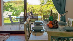 A dining table set with plates, glasses, and a bottle, with a view of an outdoor patio. - Villa Camilla: Private Pool & BBQ, Panoramic Garden Near Le Saline beach (Punta de Su Turrione)
