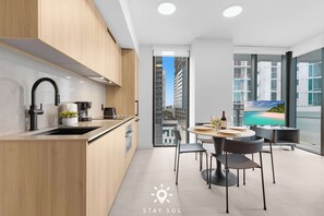 A modern kitchen with a sink, stove, and dining area with chairs and a table. - City‑View 1BR  | Modern & Refined (Miami)