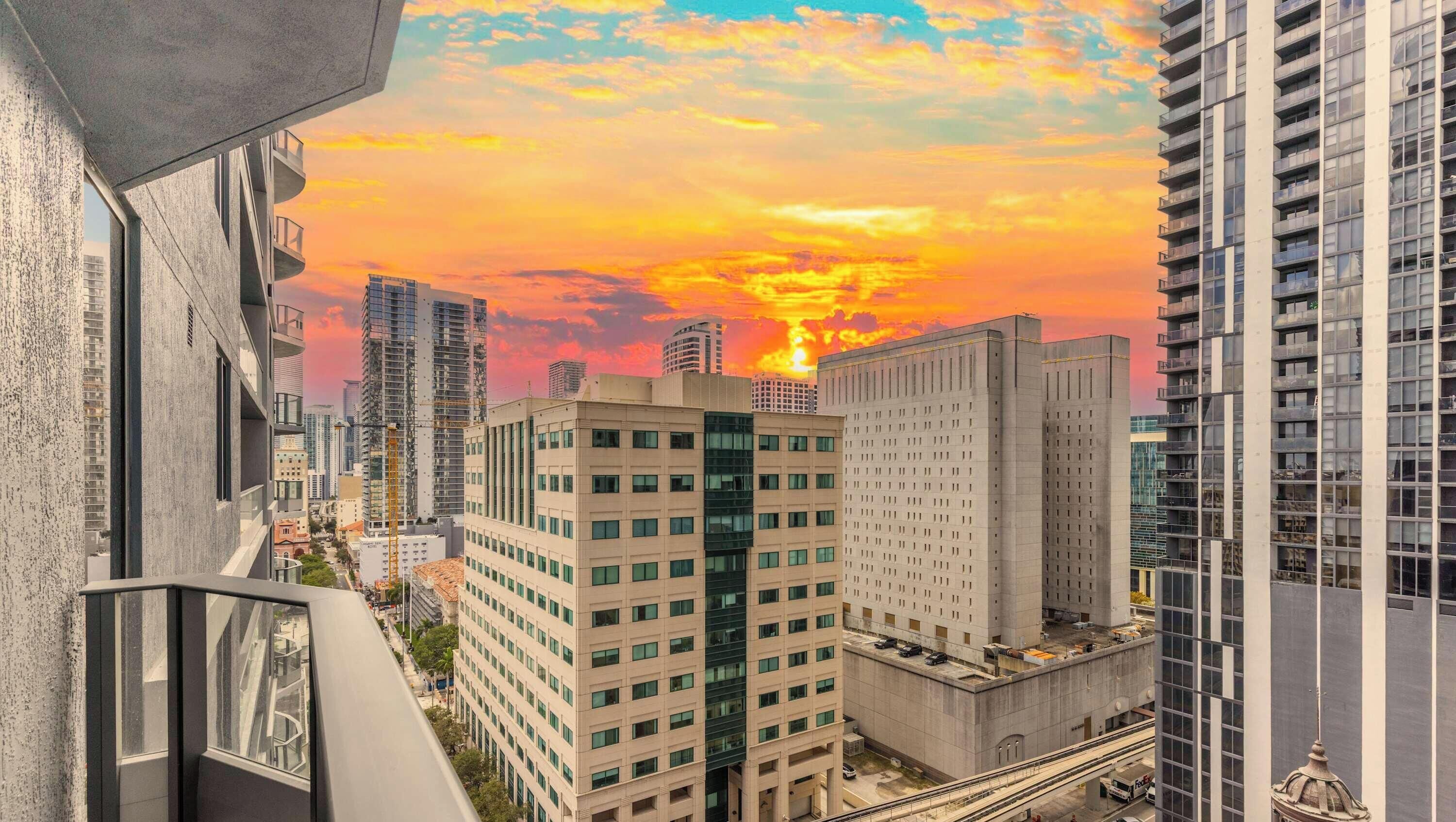 A high-rise building with a view of the sunset, other buildings, and a street below.