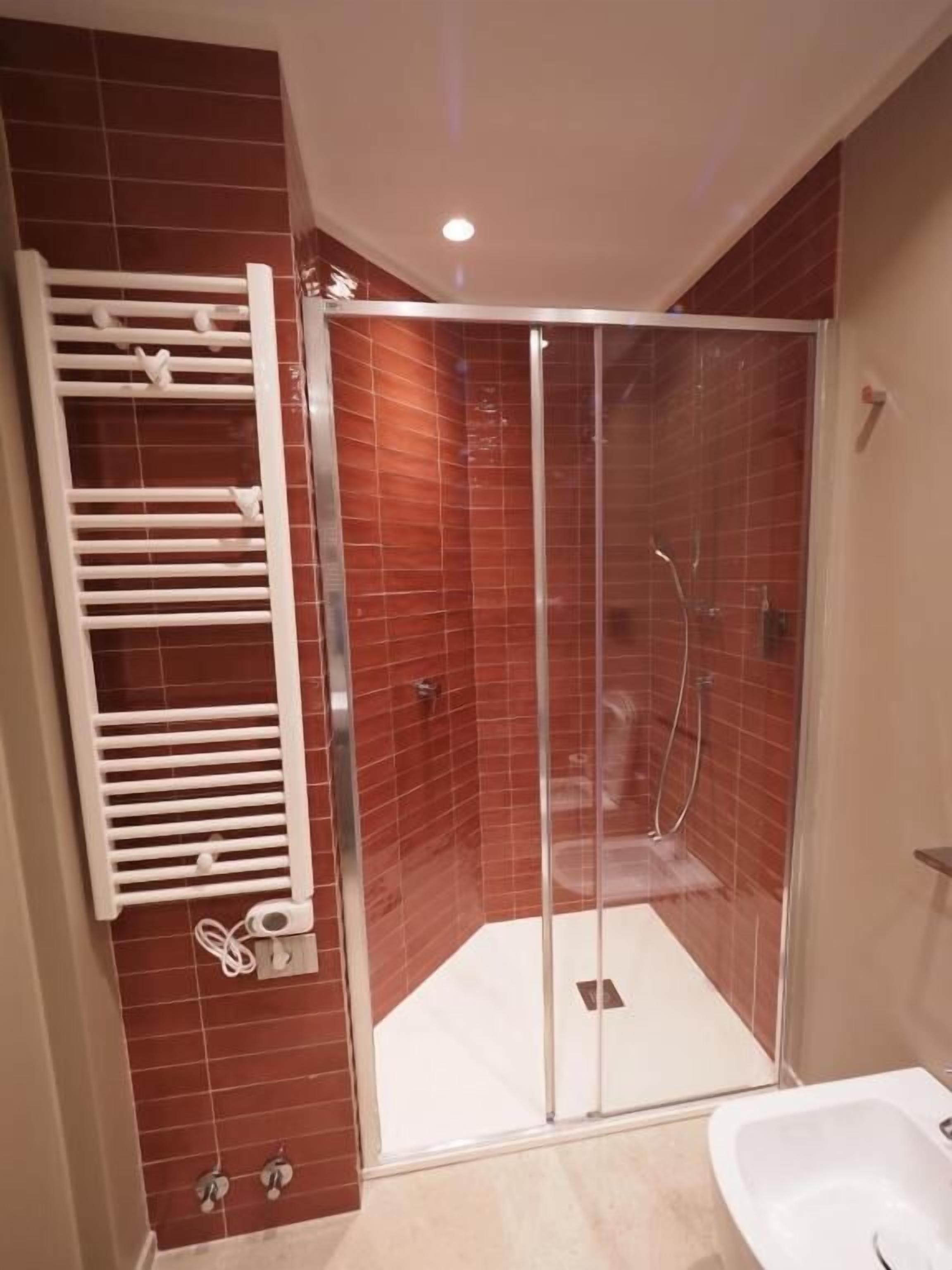 A shower with glass doors, a white towel rack, and a white bathtub.