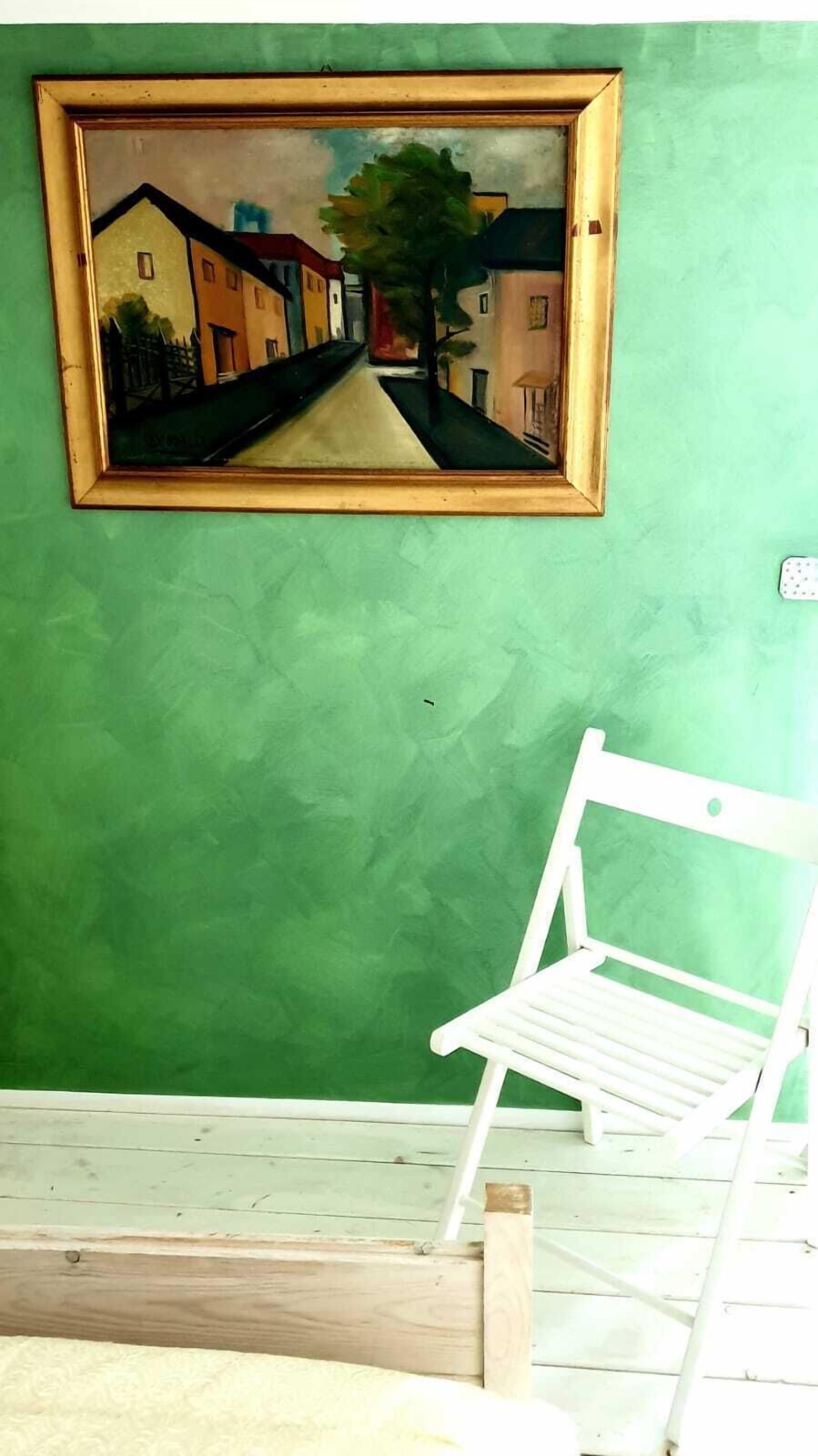 A room with a green wall, a framed painting, and a white chair.