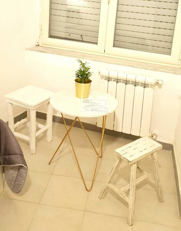 Une petite pièce avec une table blanche, un petit tabouret, une plante en pot et un radiateur.