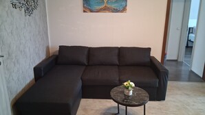 Un salon moderne avec un canapé d’angle, une table basse ronde ornée d’un vase de fleurs et un tableau accroché au mur.