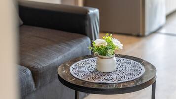 A round table with a decorative plate, a white vase with flowers, and a grey sofa in the background.