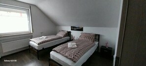Une chambre avec deux lits simples, une fenêtre et un radiateur.