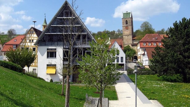 Un bâtiment doté d’un toit triangulaire, d’une tour horloge et de maisons traditionnelles en arrière-plan.