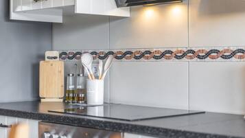 A kitchen with a modern design, featuring a black countertop, a wooden cutting board, and a white utensil holder with various kitchen tools.