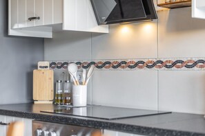 Une cuisine au design moderne, dotée d’un plan de travail noir, d’une planche à découper en bois et d’un porte-ustensiles blanc contenant divers outils de cuisine.