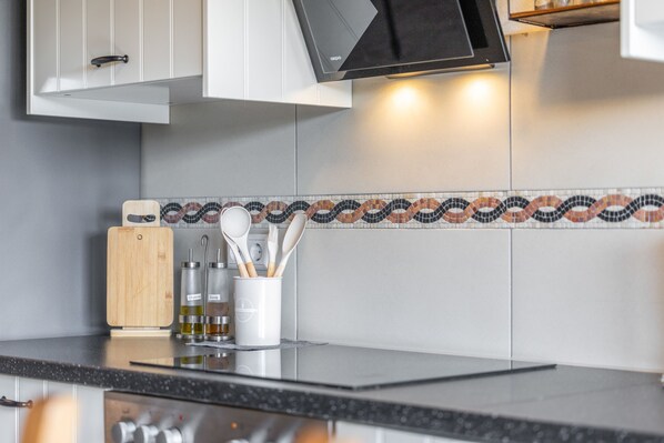 A kitchen with a modern design, featuring a black countertop, a wooden cutting board, and a white utensil holder with various kitchen tools.