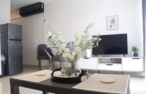 Et moderne køkken med et køleskab, et spisebord med servietter, en vase med blomster, et fladskærms-TV og en lille potteplante på TV-møblet.