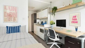Ein modernes Schlafzimmer mit einem Bett, einem Schreibtisch und einem Computer. An den Wänden hängen zwei Gemälde und auf dem Schreibtisch steht eine grüne Pflanze.
