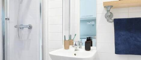 Une salle de bain avec un lavabo blanc, une cabine de douche en verre, un porte-serviettes et un miroir.