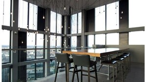 Ein modernes Interieur mit einem langen Tisch, Barhocker, großen Fenstern und hängenden Lampen.