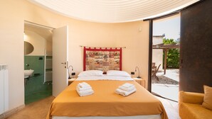 Ein Schlafzimmer mit einem Bett, zwei Nachttischen, einem Fenster und einem Badezimmer mit Waschbecken und Spiegel.