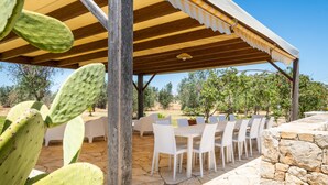 Eine Terrasss mit weißen Stühlen und Tischen, einer Holz-Pergola und einer Kakteenpflanze.