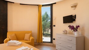 Ein Schlafzimmer mit Bett, Sofa, Schminktisch, Fernseher und einem Fenster mit Vorhängen.