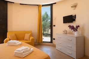 Ein Schlafzimmer mit Bett, Sofa, Schminktisch, Fernseher und einem Fenster mit Vorhängen.
