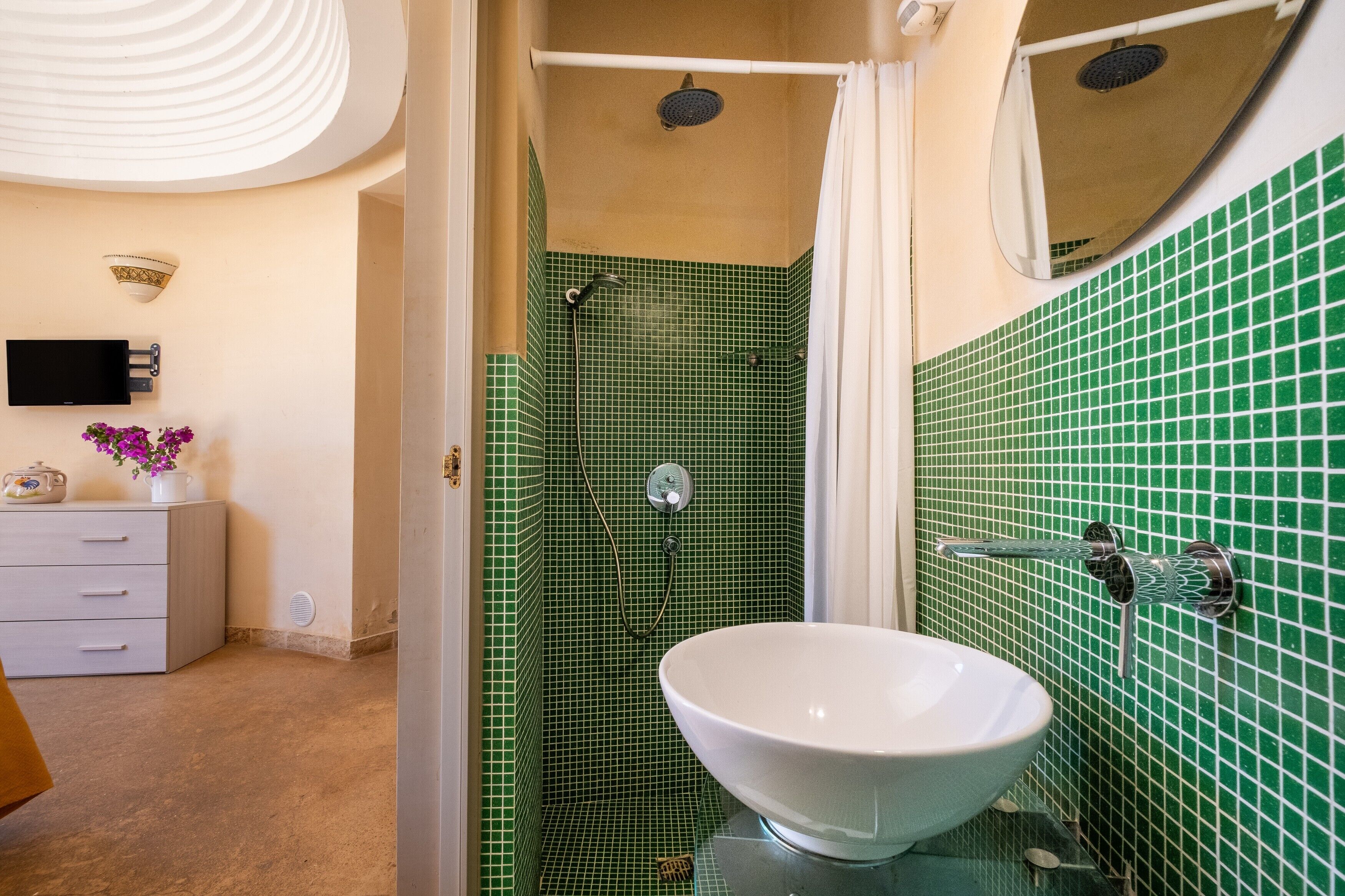 Ein Badezimmer mit einer grüngestühlten Dusche, einem weißen Waschbecken und einem an der Wand befestigten Flachbildfernseher.
