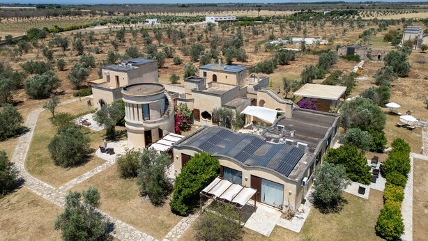 A residential area with multiple buildings, including a house with a curved roof and solar panels, surrounded by olive trees and a clear sky. - Room 'Residenze Uliveto - Residence 15, Private Terrace and Air Conditioning (Nardò)