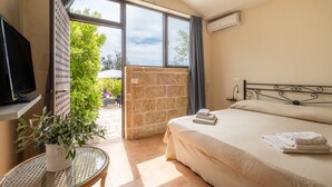 A hotel room with a bed, a TV, a small table with a plant, and a view of the outdoors. - Room 'Residenze Uliveto - Residenza 8' with Shared Pool, Private Terrace and Air Conditioning (Nardò)