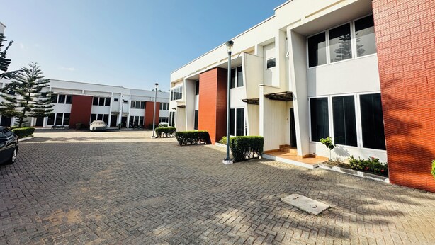 Um edifício moderno com um pátio pavimentado, janelas amplas e uma combinação de tijolos e paredes brancas.