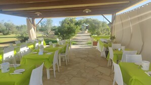 An outdoor dining area with tables covered in green tablecloths and white chairs, arranged in rows with a stone floor. - Apartment 'Residenze Uliveto - Residenza 10' Private Terrace and Air Conditioning (Nardò)