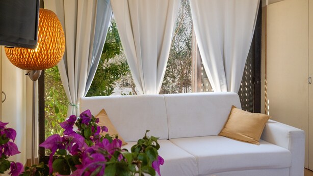 A white sofa with a beige pillow, a wooden table, and purple flowers in the foreground. - Apartment 'Residenze Uliveto - Residenza 10' with Pool, Private Terrace and Air Conditioning (Nardò)