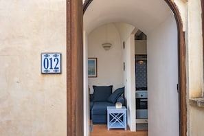 Ein schmaler Flur mit einer blauen Tür, einer Nummernschild und einem kleinen Tisch mit einer Lampe sowie einem Sofa mit Kissen.