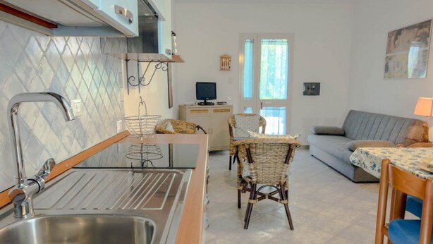 A kitchen with a sink, dining area with chairs, a sofa, and a television. - Casa Mimì (Orosei)
