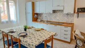 A compact kitchen with white cabinets, a tiled backsplash, and a dining table set for four. - Casa Mimì (Orosei)