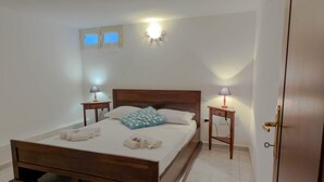 A bedroom with a wooden bed, two bedside tables with lamps, a wall-mounted light, and a door. - Casa Mimì (Orosei)