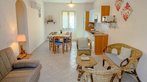 A spacious living area with a sofa, wicker chairs, a dining table, and a kitchen area with a sink and cabinets. - Casa Mimì (Orosei)