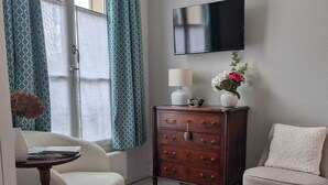 A living room with a sofa, armchair, wooden dresser, TV, and a patterned rug. - La loge Diane à deux pas du château (Chantilly)