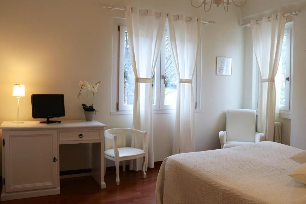 A bedroom with a bed, a desk with a computer, a chair, and a window with curtains.