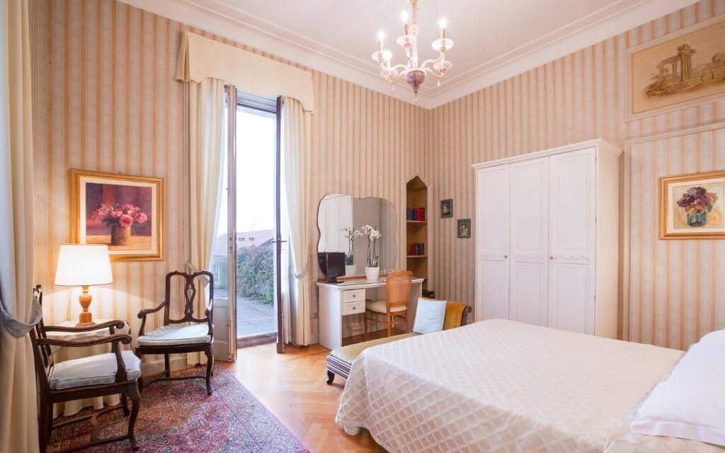 A hotel room with a bed, desk, chair, and a view through an open door.
