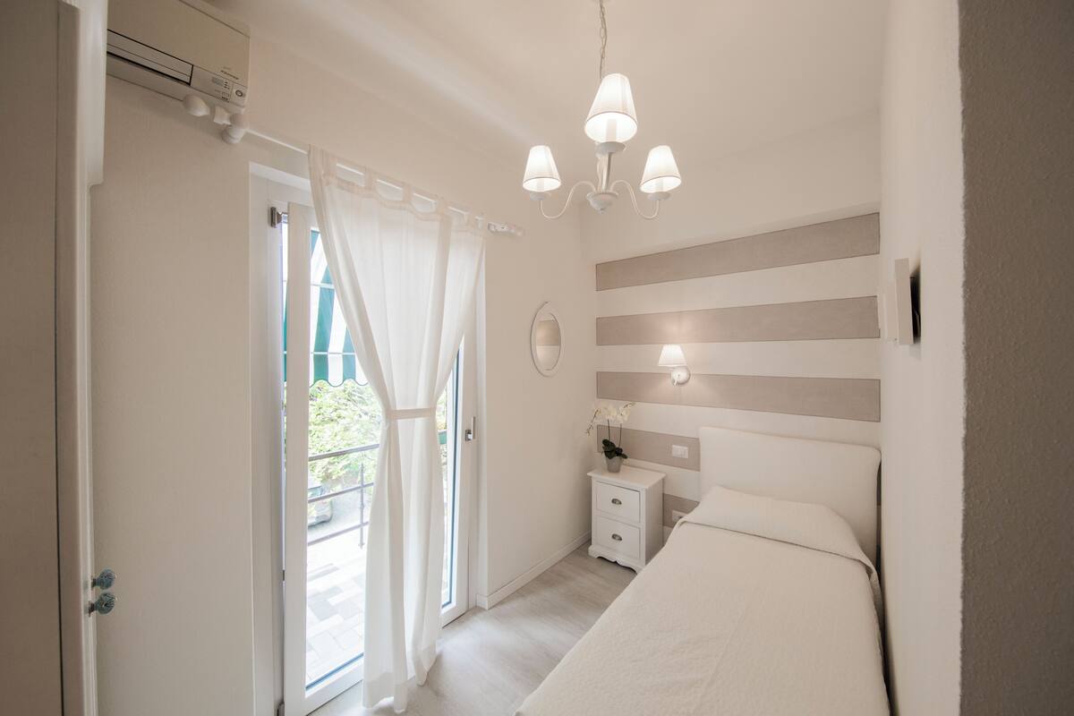 A bedroom with a bed, bedside table, lamp, and a view through a door.