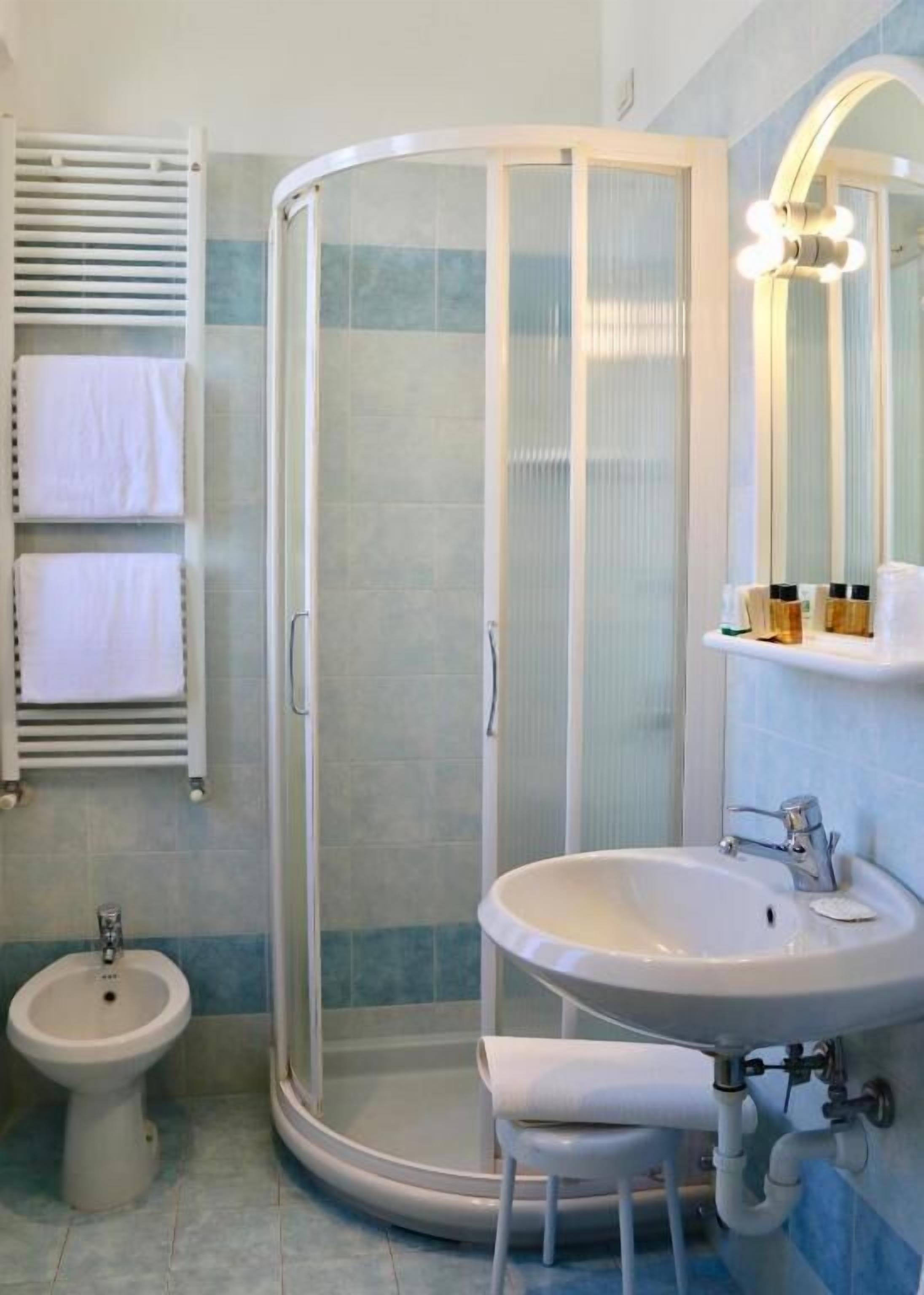 A bathroom with a glass-enclosed shower, a pedestal sink, a bidet, and a towel rack with towels.