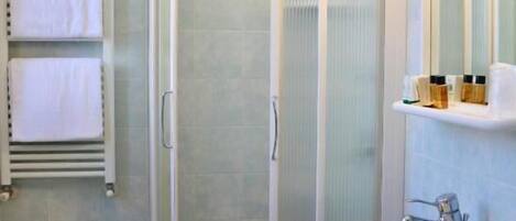 A bathroom with a glass-enclosed shower, a pedestal sink, a bidet, and a towel rack with towels.