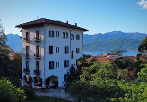 Un edificio bianco con balconi, uno sfondo montuoso e vista sul lago.